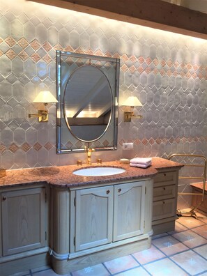 A bathroom with a large mirror, two wall-mounted lamps, a sink, and a vanity with drawers. - Villa Sawallisch (Grassau)