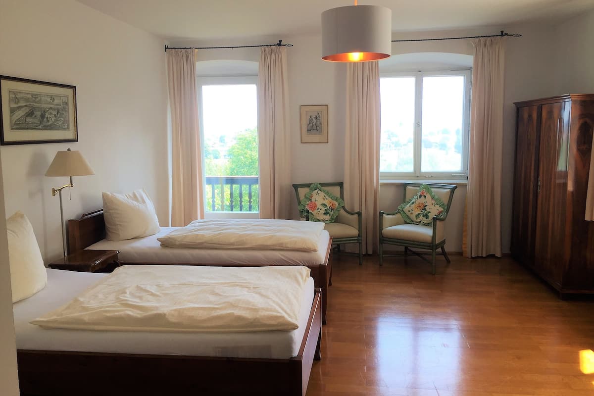A hotel room with two beds, a desk, a chair, a wardrobe, and a balcony with curtains.