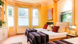 Una camera d'albergo con due letti, un'ampia finestra, un termosifone, una scrivania e una lampada.