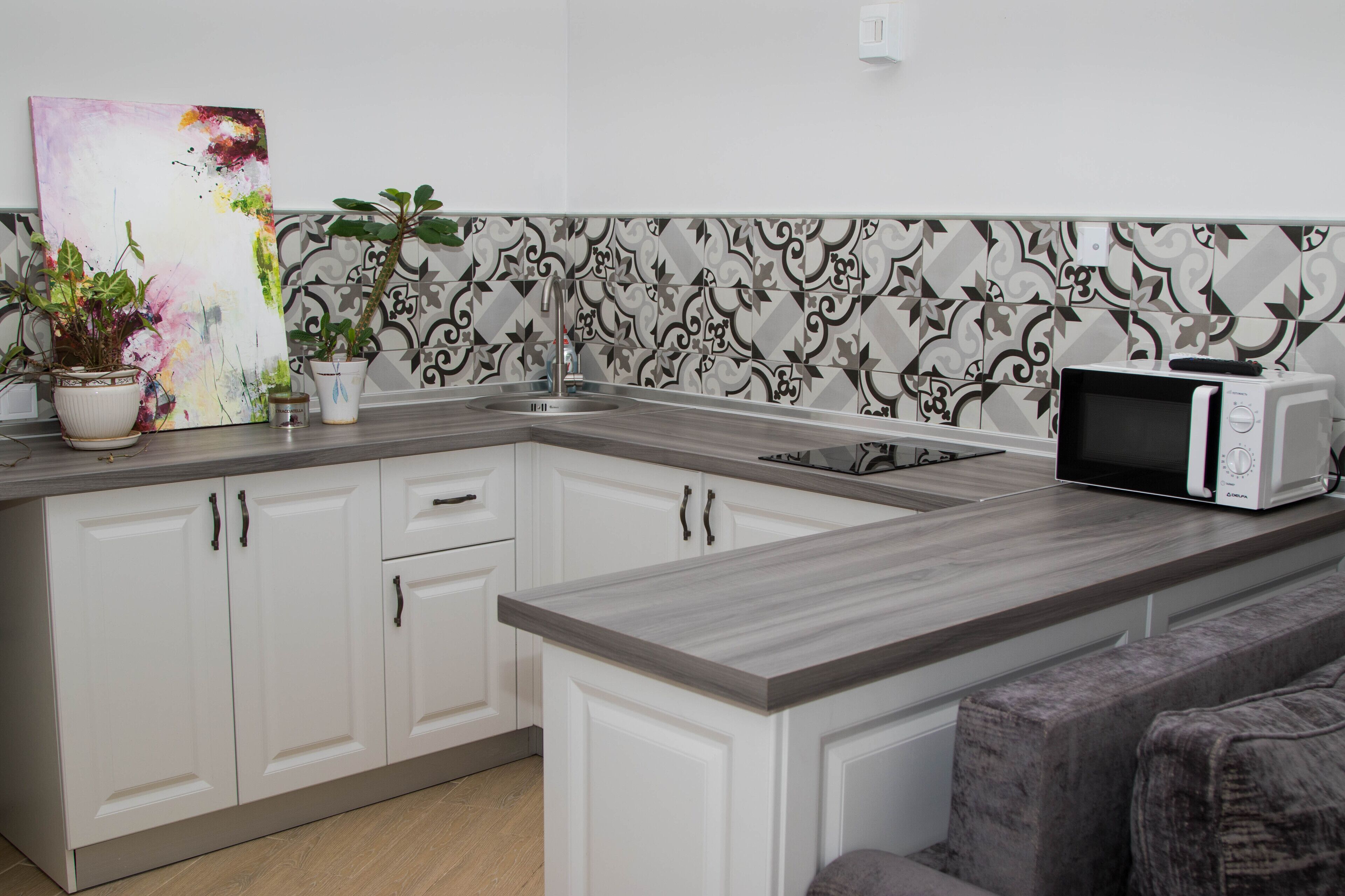 A modern kitchen with white cabinets, a grey countertop, a microwave, and a decorative backsplash.