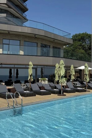 Un hotel moderno con zona de piscina, tumbonas y sombrillas.