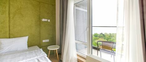 Habitación de hotel con cama, una mesita redonda, un radiador y un balcón con una silla.