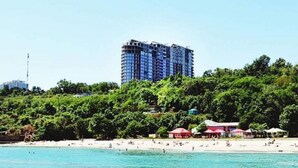 Une plage avec un grand bâtiment en arrière-plan, entourée de verdure.