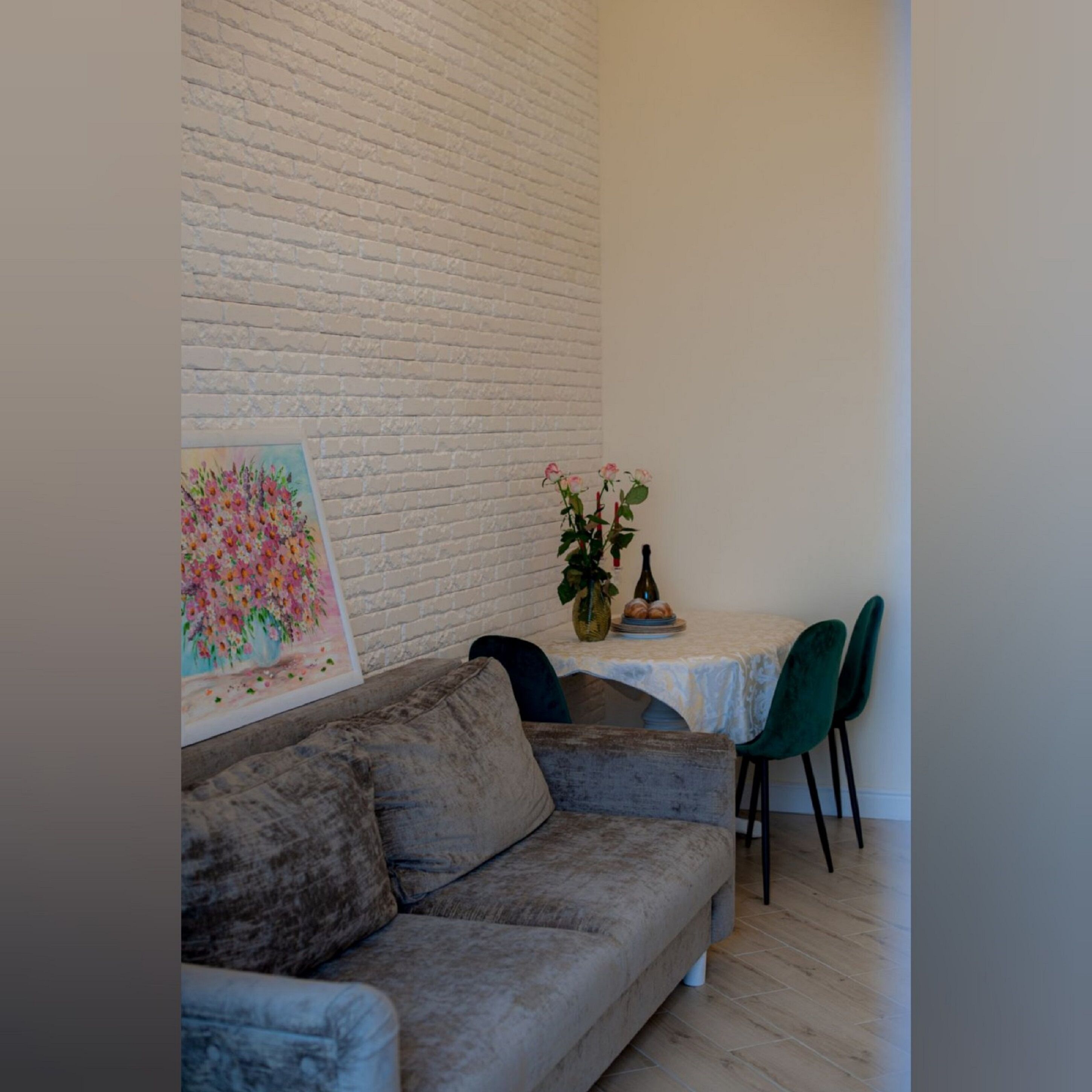 Un salon chaleureux avec un canapé gris, une petite table sur laquelle est posé un vase de fleurs et un tableau représentant des fleurs accroché au mur.
