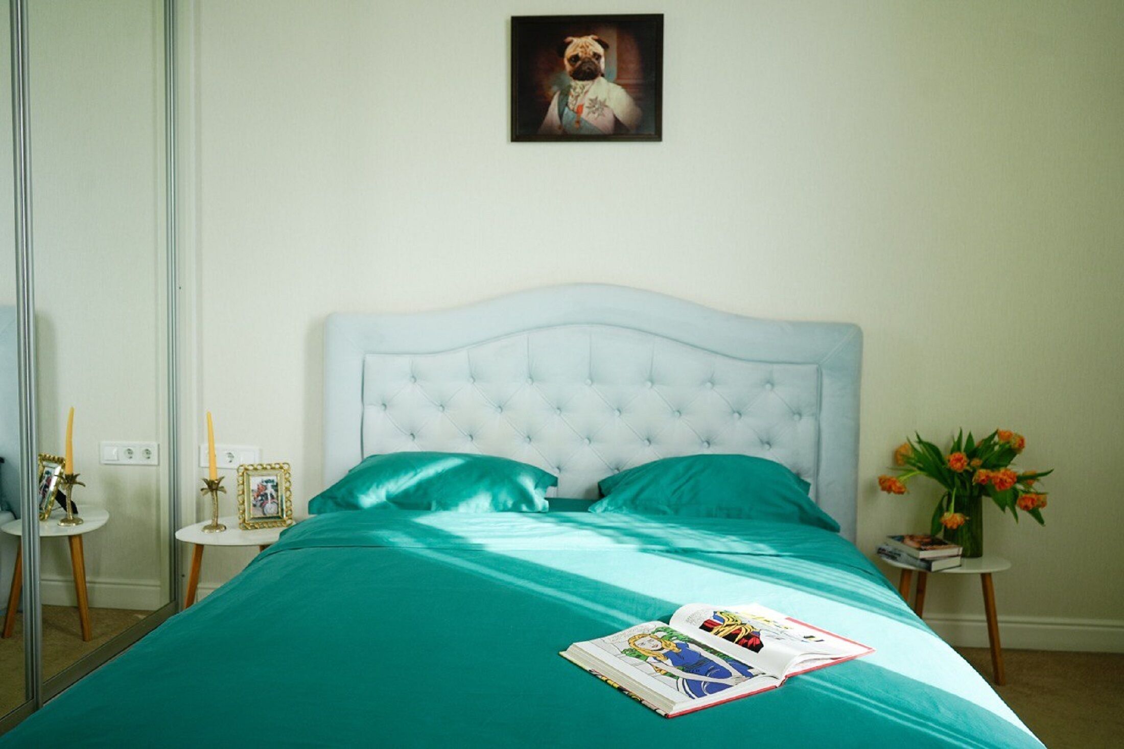 A bedroom with a bed, a bedside table, a mirror, and a framed picture on the wall.