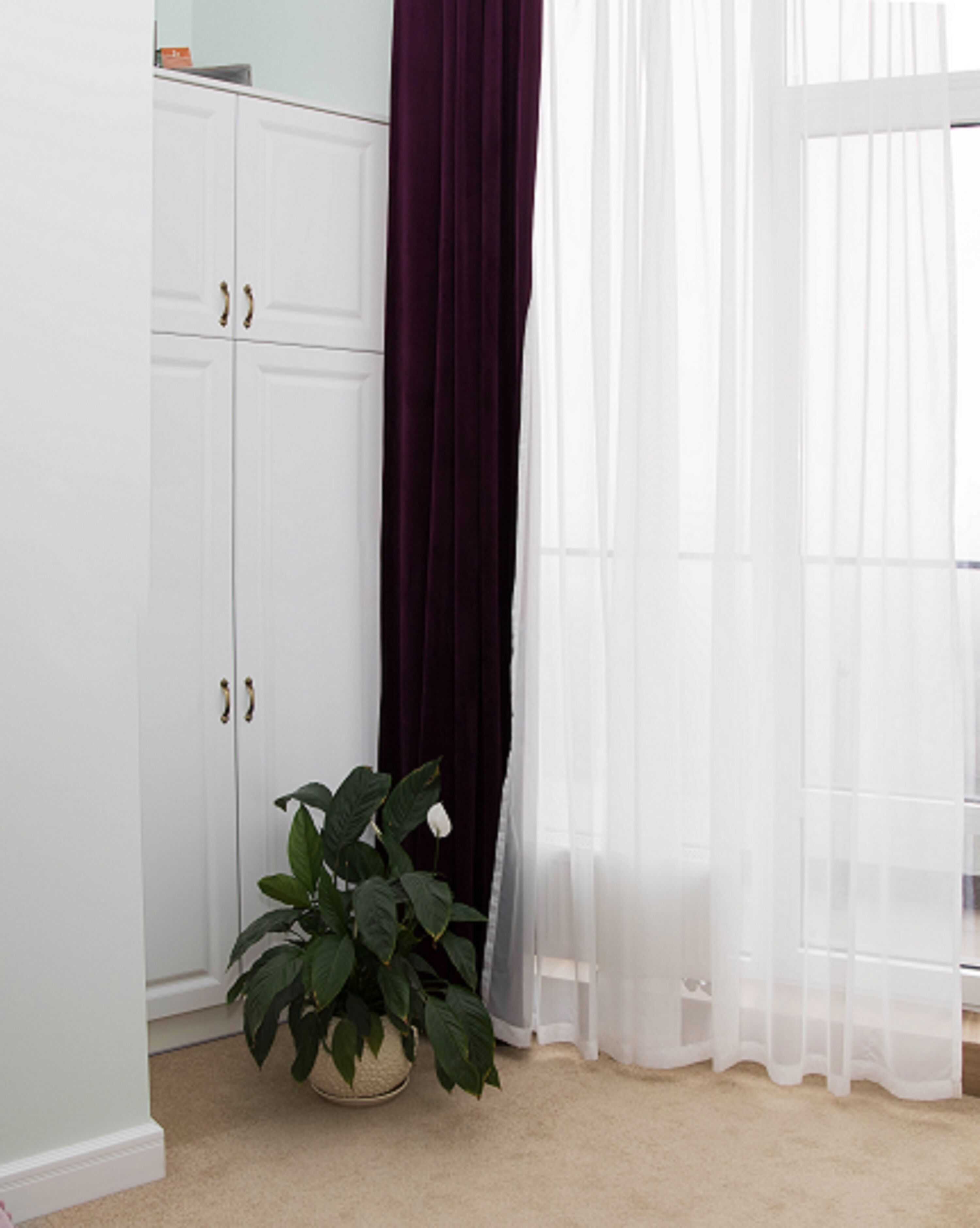 Una habitación con un armario blanco, una planta en maceta y cortinas blancas traslúcidas.