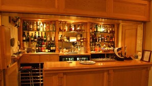 A bar area with wooden cabinets, shelves stocked with various liquor bottles, a bar counter, and a wine rack. - Haigs Hotel (Solihull)