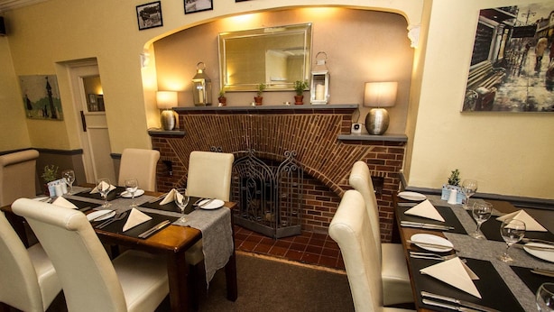 A dining area with a brick fireplace, tables set with plates and cutlery, and chairs. - Haigs Hotel (Solihull)