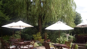 Outdoor patio seating with umbrellas, surrounded by lush greenery and trees. - Haigs Hotel (Solihull)