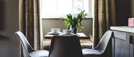 A dining area with a table, two chairs, a potted plant, and a window with curtains.