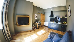 Uma sala de estar moderna com sofá, televisão na parede, área de jantar com mesa e cadeiras e cozinha equipada.