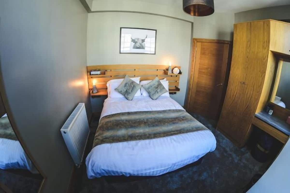 Quarto com cama, abajures, guarda-roupa de madeira, quadro emoldurado na parede e radiador.