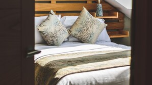 Quarto com cabeceira de madeira, cama com roupa de cama branca e um claraboia acima.