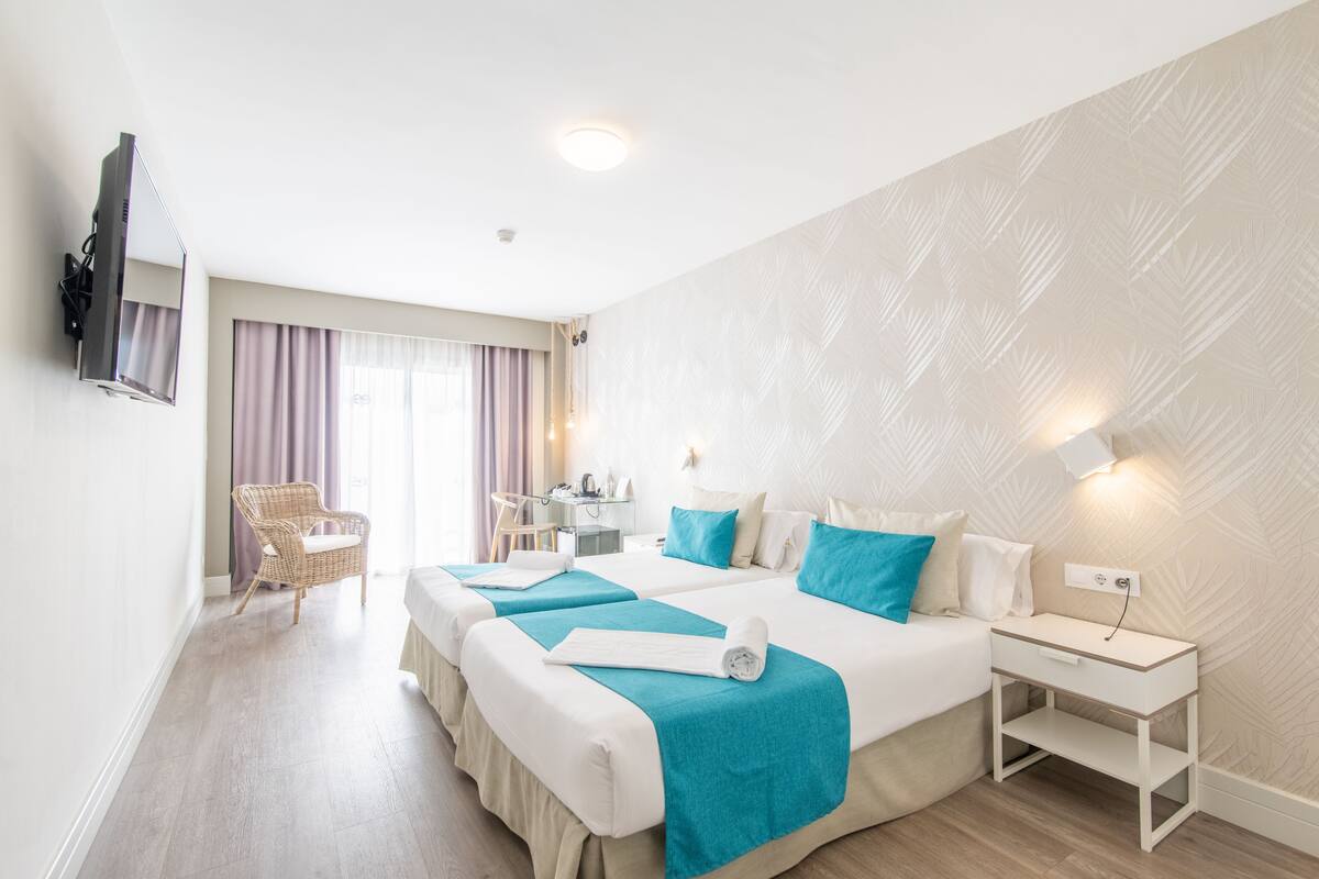 Ein Hotelzimmer mit zwei Betten, einem Fernseher, einem Schreibtisch und einem Stuhl.