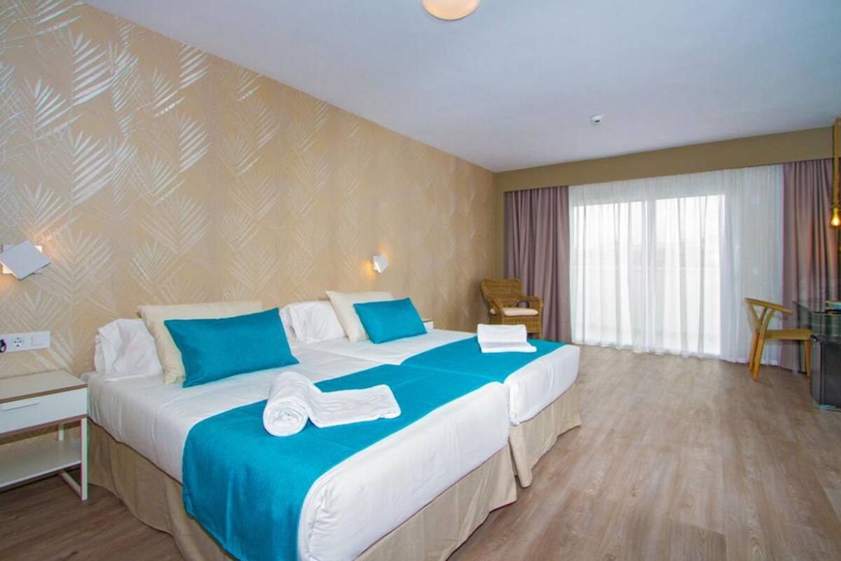 Ein Hotelzimmer mit zwei Betten, einem Schreibtisch, einem Stuhl und einem großen Fenster mit Vorhängen.