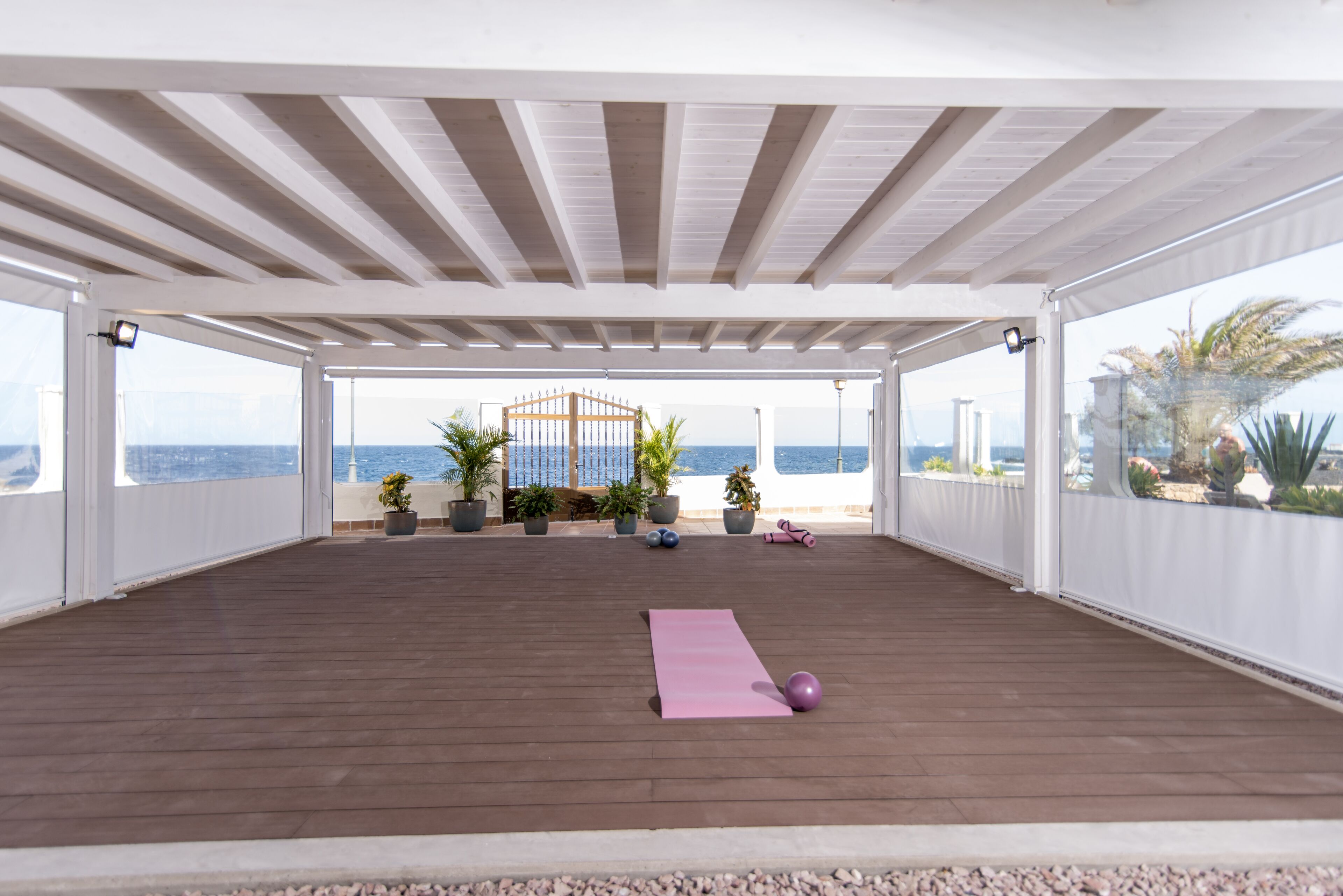 Un espacio al aire libre cubierto con una terraza de madera, colchoneta para ejercicios y balones de gimnasia.