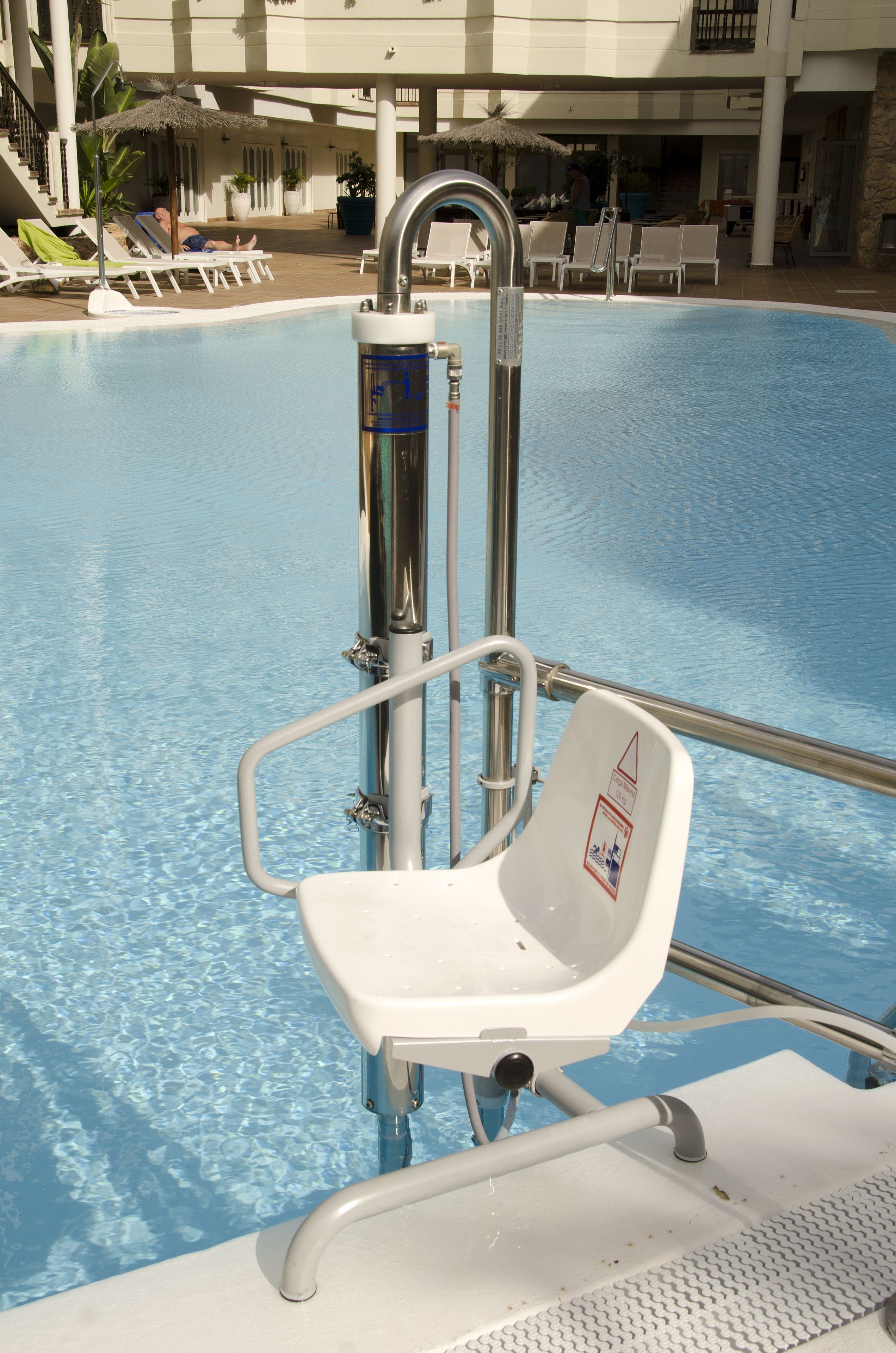 Zona junto a la piscina con una silla de salvavidas, sillas de piscina y un quiosco de techo de paja.