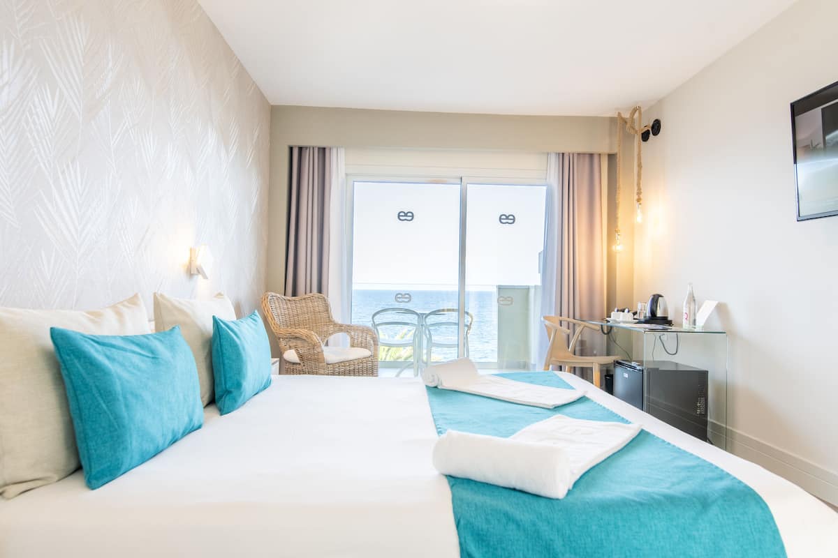 Ein Hotelzimmer mit einem großen Bett, zwei Stühlen, einem Schreibtisch und Meerblick.