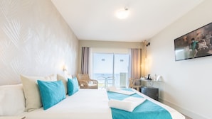 A hotel room with a large bed, a desk, a chair, and a view of the sea through the window. - Hotel Ereza Mar- Adults Only (Antigua)