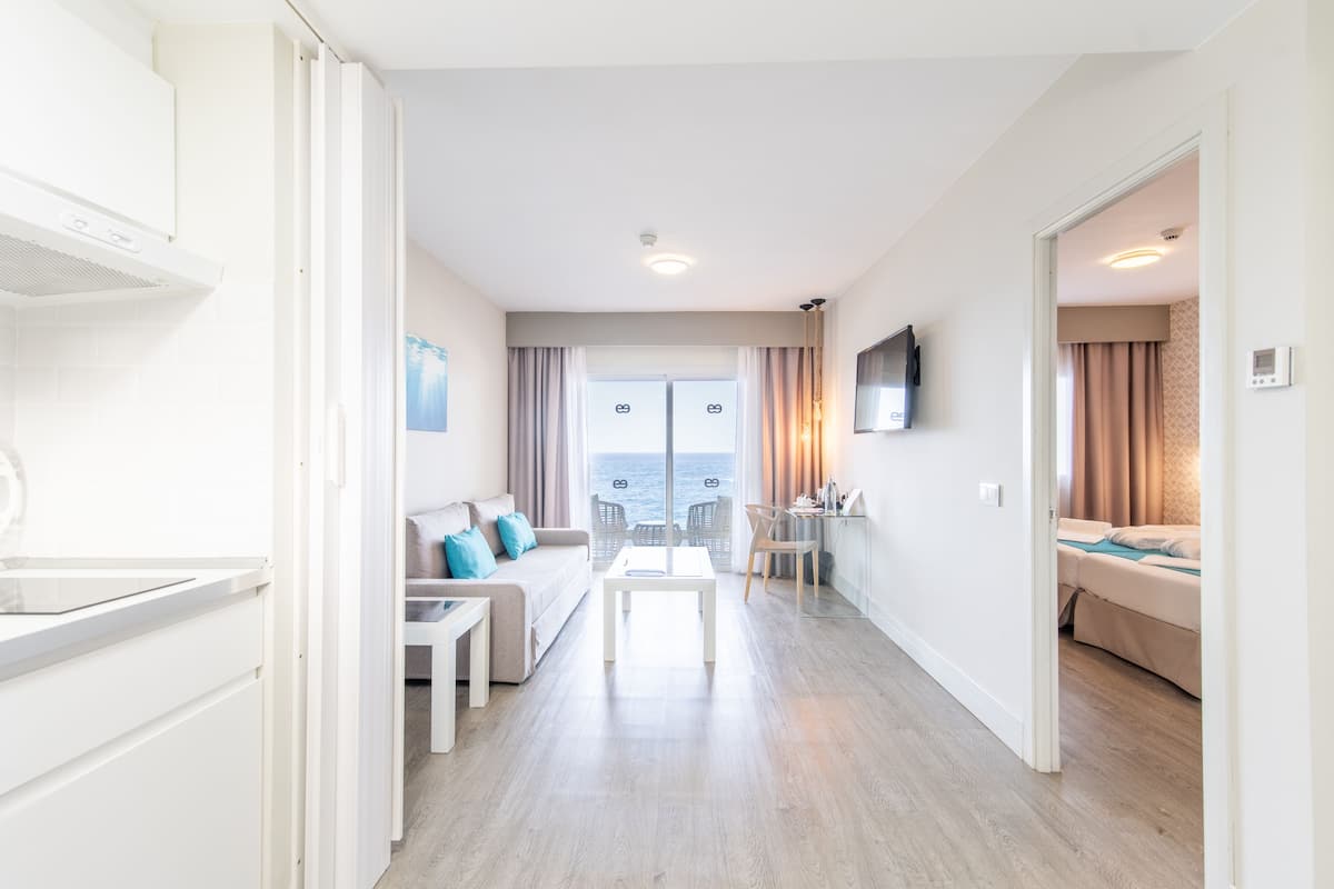 Ein modernes Hotelzimmer mit Balkon, einer Couch, einem Esstisch und einem an der Wand befestigten Fernseher.