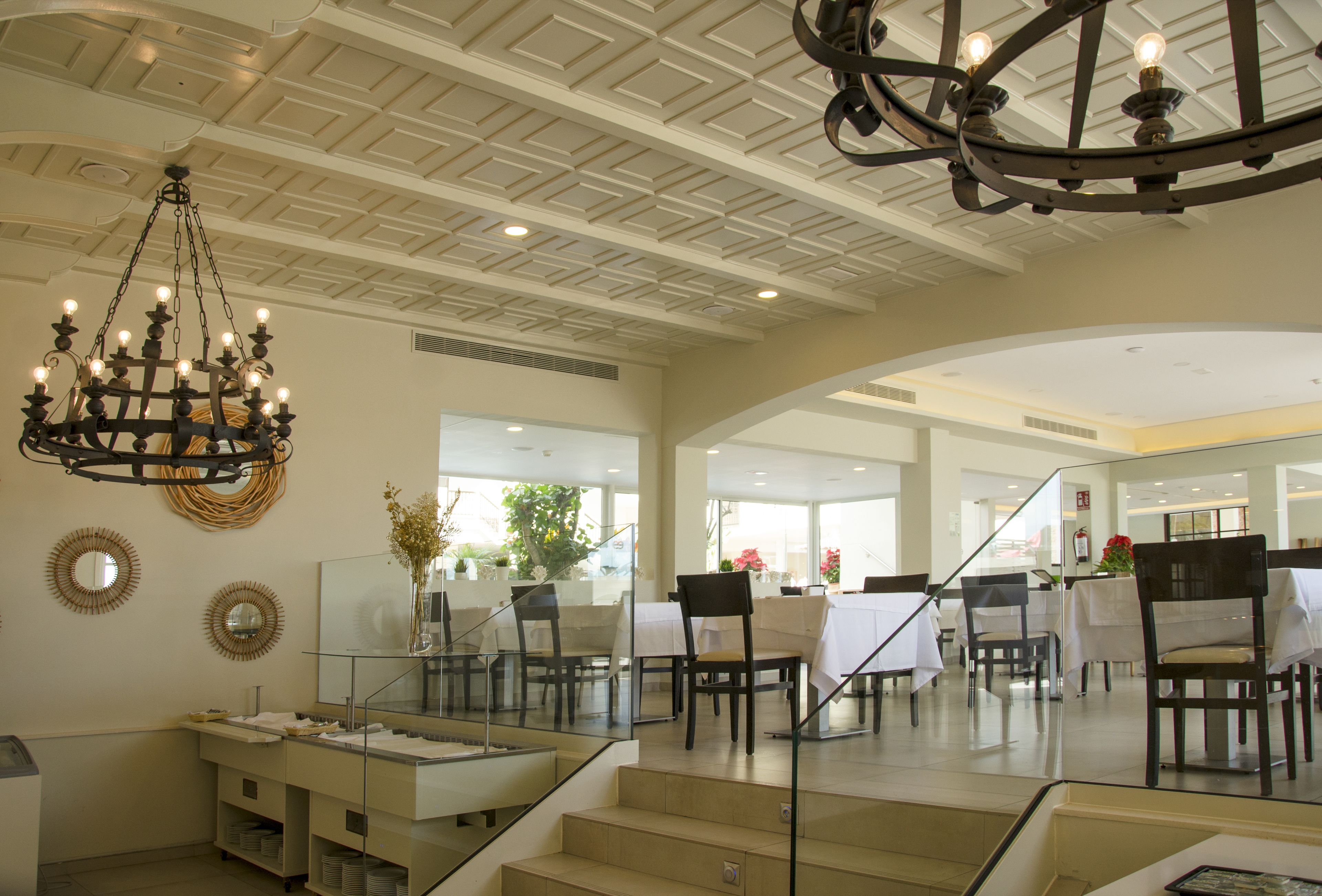 A spacious hotel lobby with a grand chandelier, a staircase leading to upper floors, and a dining area with tables and chairs.
