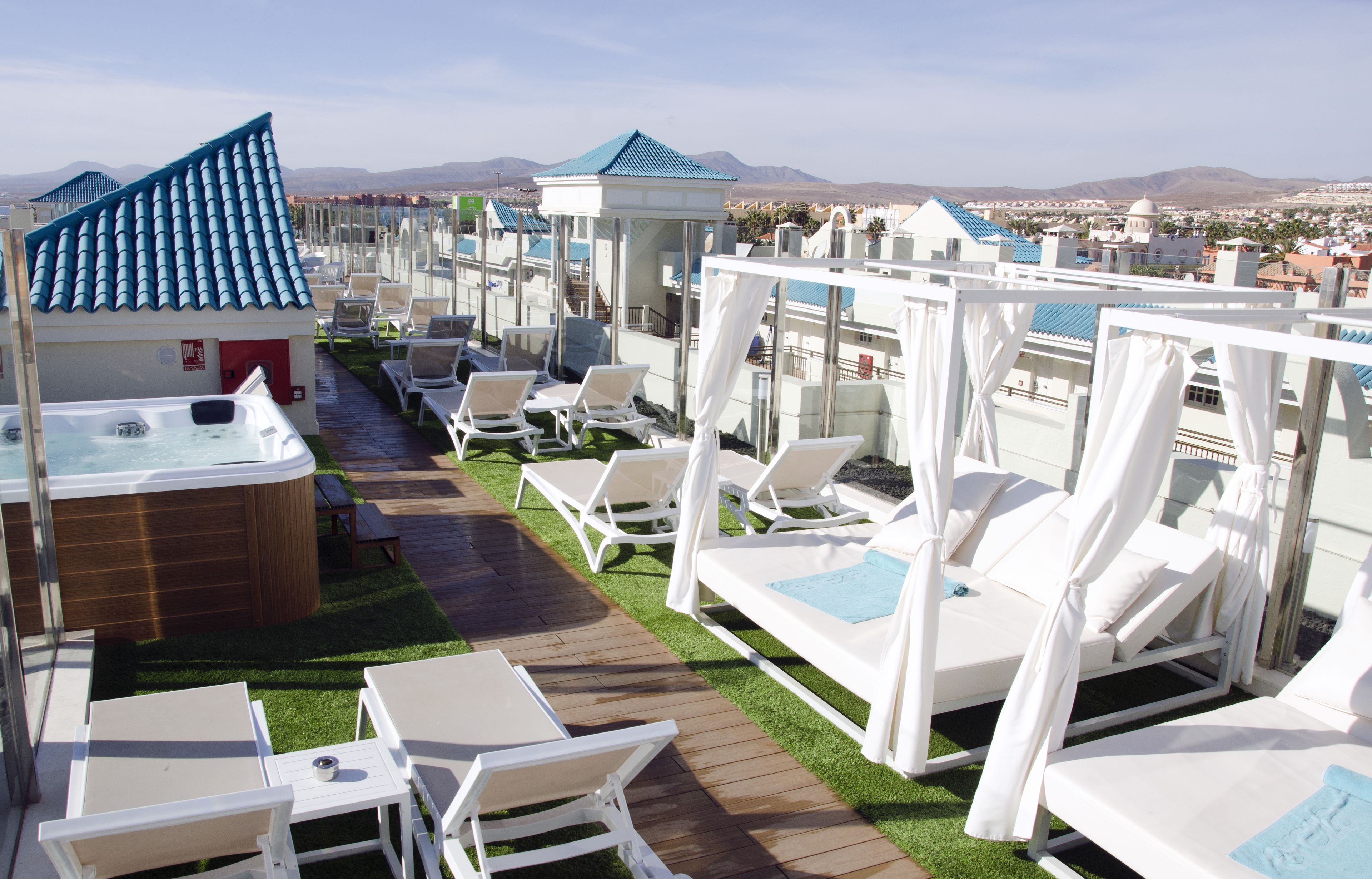 A rooftop lounge area with sun loungers, a hot tub, and a view of the cityscape.