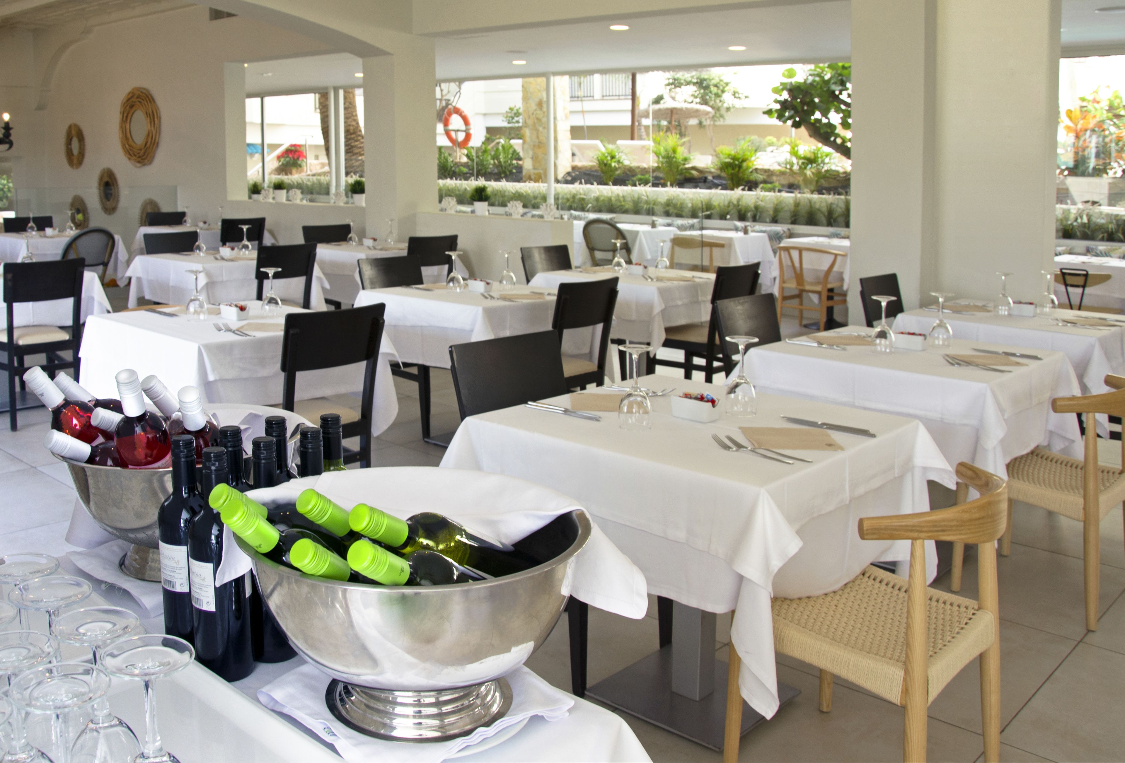 Een restaurant met meerdere gedekte tafels, elk met een witte tafelkleed en bestek.