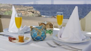 A table set with plates, glasses, and a basket of bread, overlooking a coastal view. - Hotel Ereza Mar- Adults Only (Antigua)