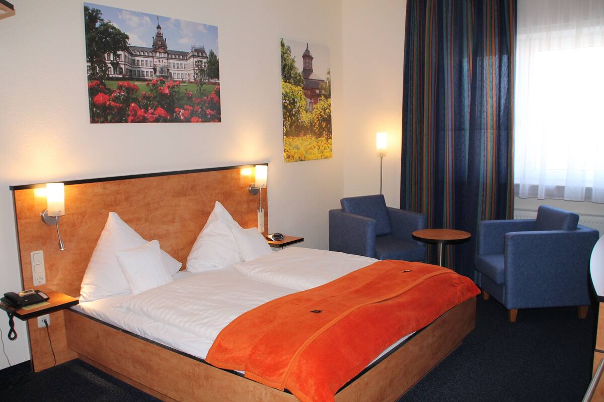 A hotel room with a large bed, two armchairs, a small table, and two wall-mounted lamps.