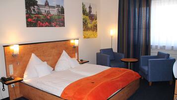 Ein Hotelzimmer mit einem großen Bett, zwei Sesseln, einem kleinen Tisch und zwei Wandleuchten.