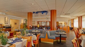 En restaurant med forskellige siddepladser, blandt andet borde og sofaer, samt en bar i baggrunden.