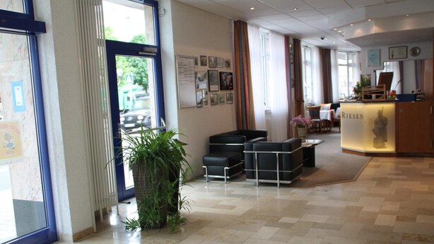 Et hotel lobby med reception, siddeområde og et stort vindue med udsigt til gaden.