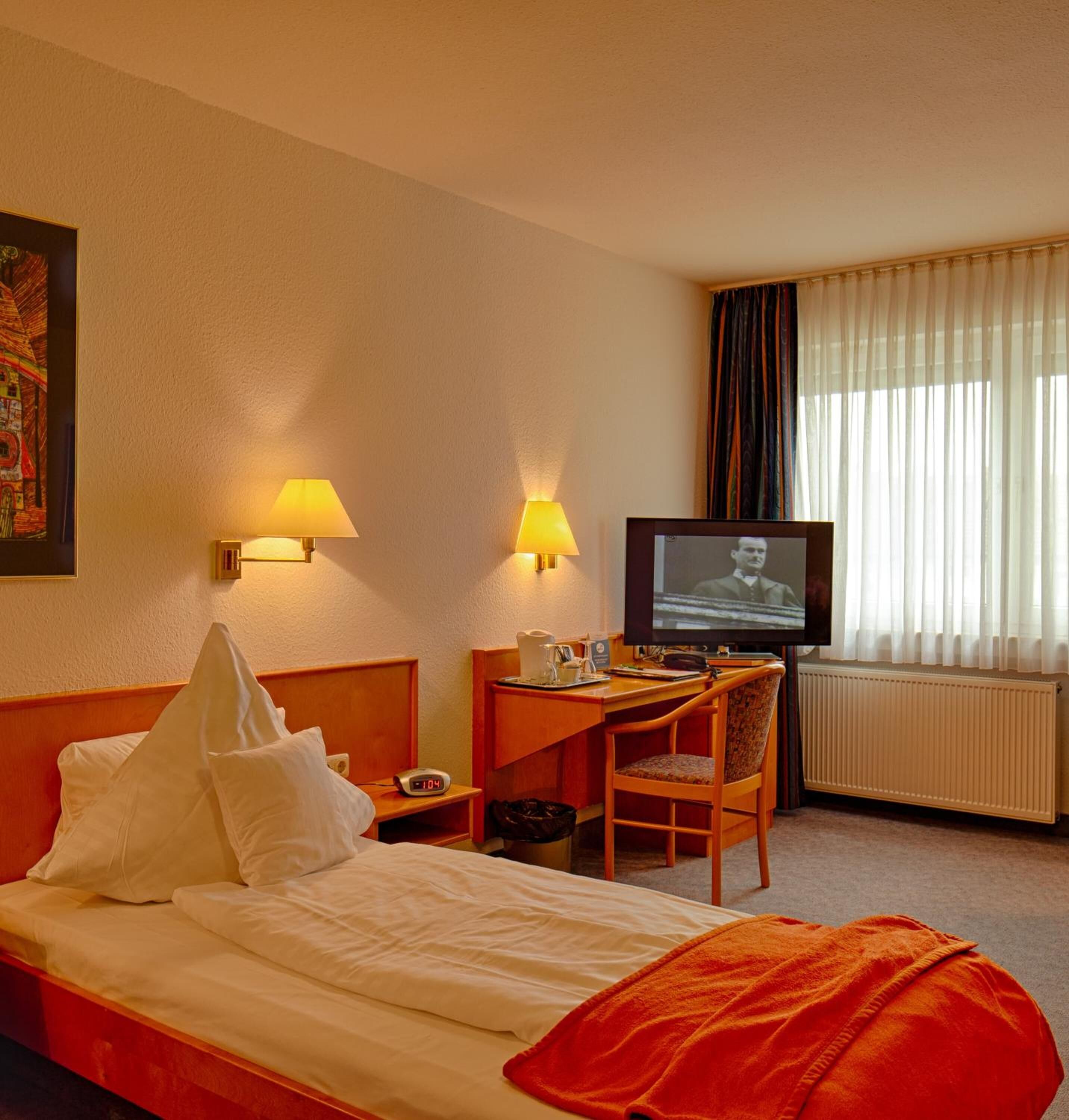 Hotelkamer met een bed, een bureau met stoel, een televisie en een raam met gordijnen.