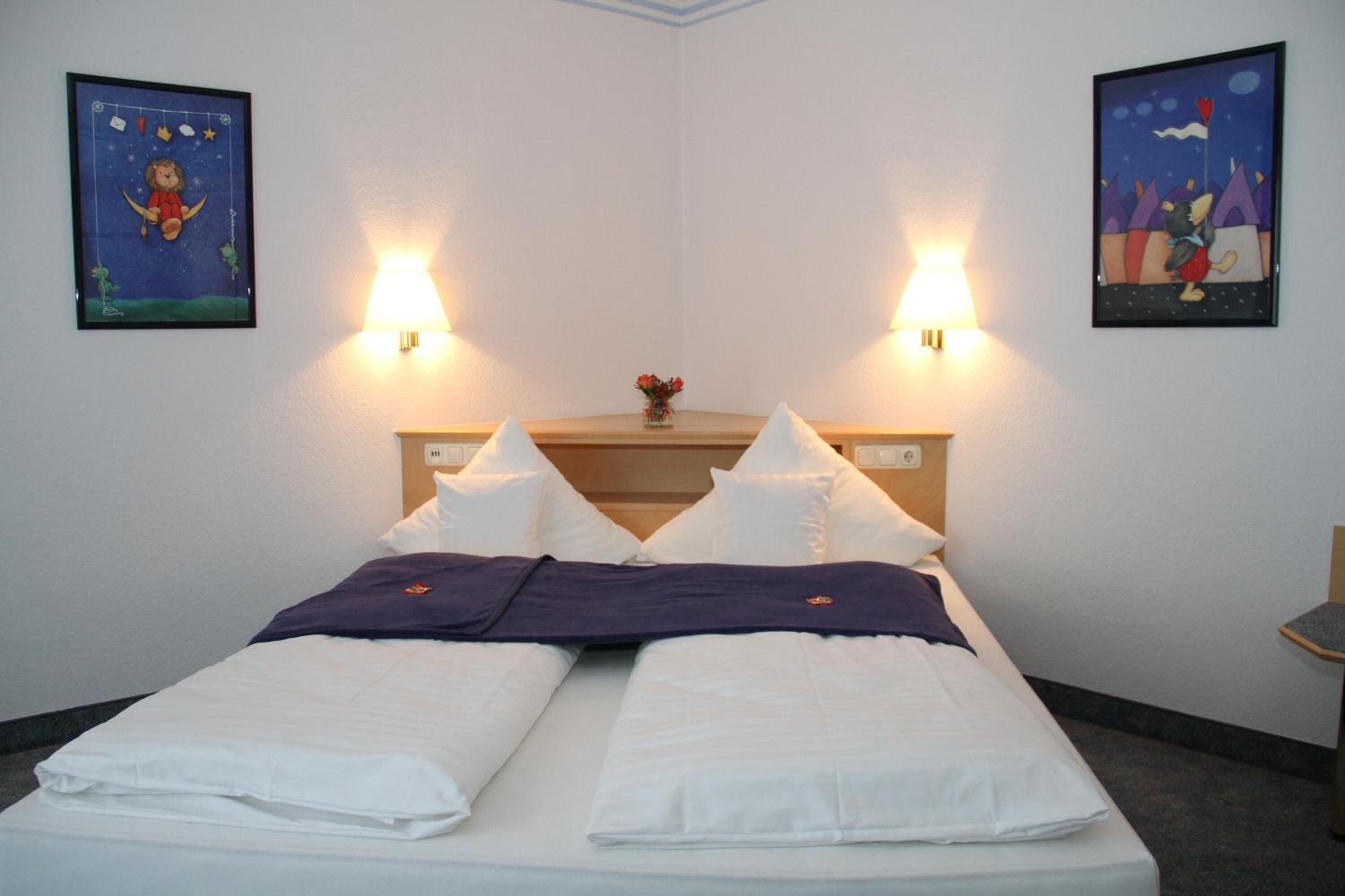 A hotel room with a bed, two wall-mounted lamps, and two framed pictures.