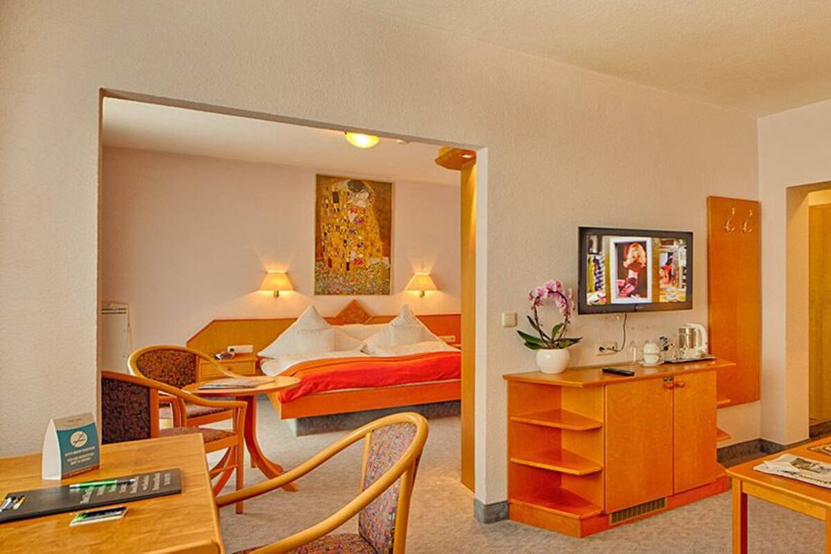 A hotel room with a bed, a desk, a chair, a sofa, a TV, and a lamp.