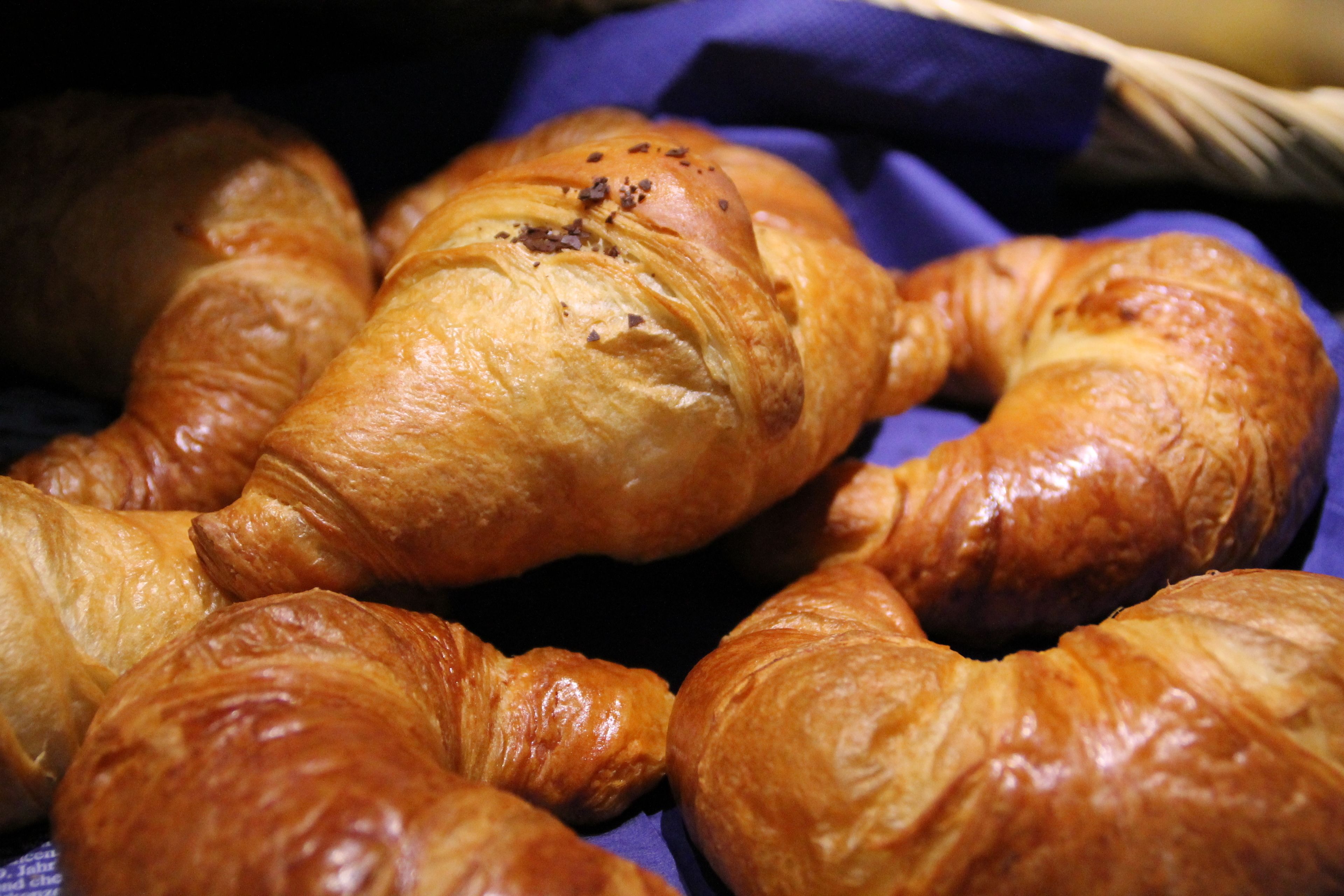 Una cesta de croissants dorados y brillantes, dispuestos sobre un paño azul.