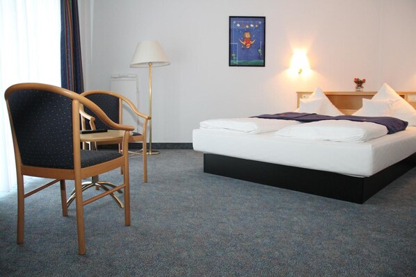 Une chambre d’hôtel avec un lit, une chaise, une lampe et un luminaire fixé au mur.