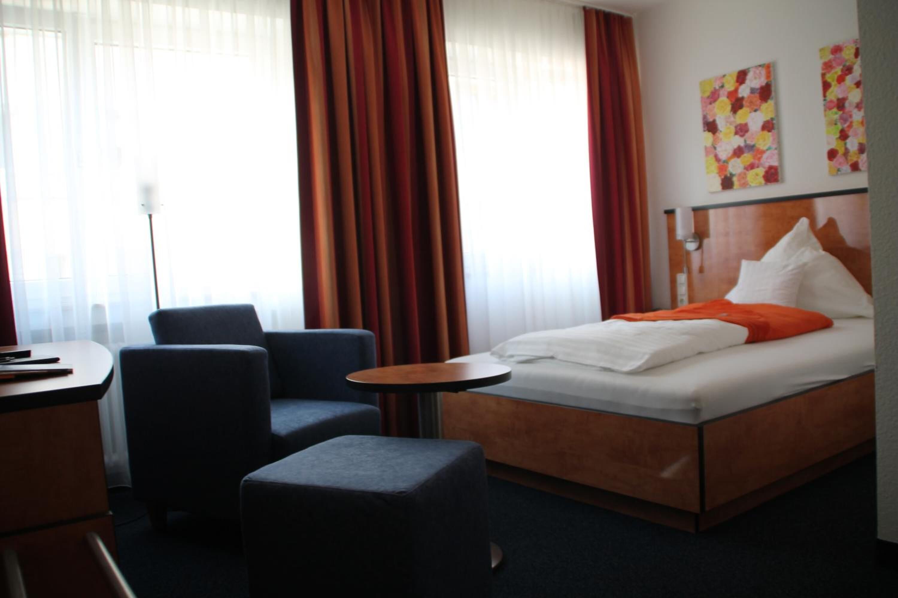 A hotel room with a bed, a desk, two chairs, a small table, and curtains.
