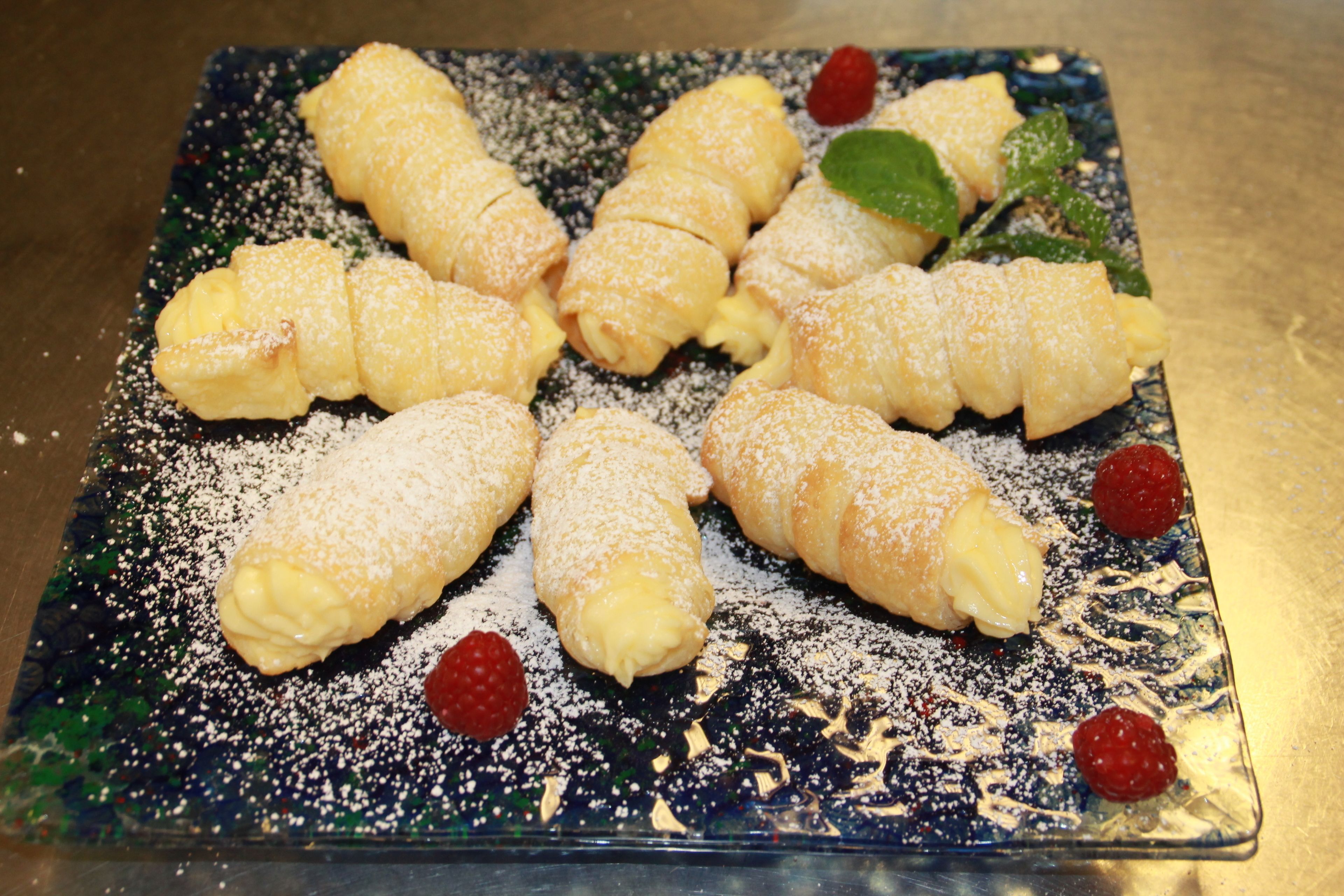 A plate of pastries dusted with powdered sugar and garnished with raspberries.