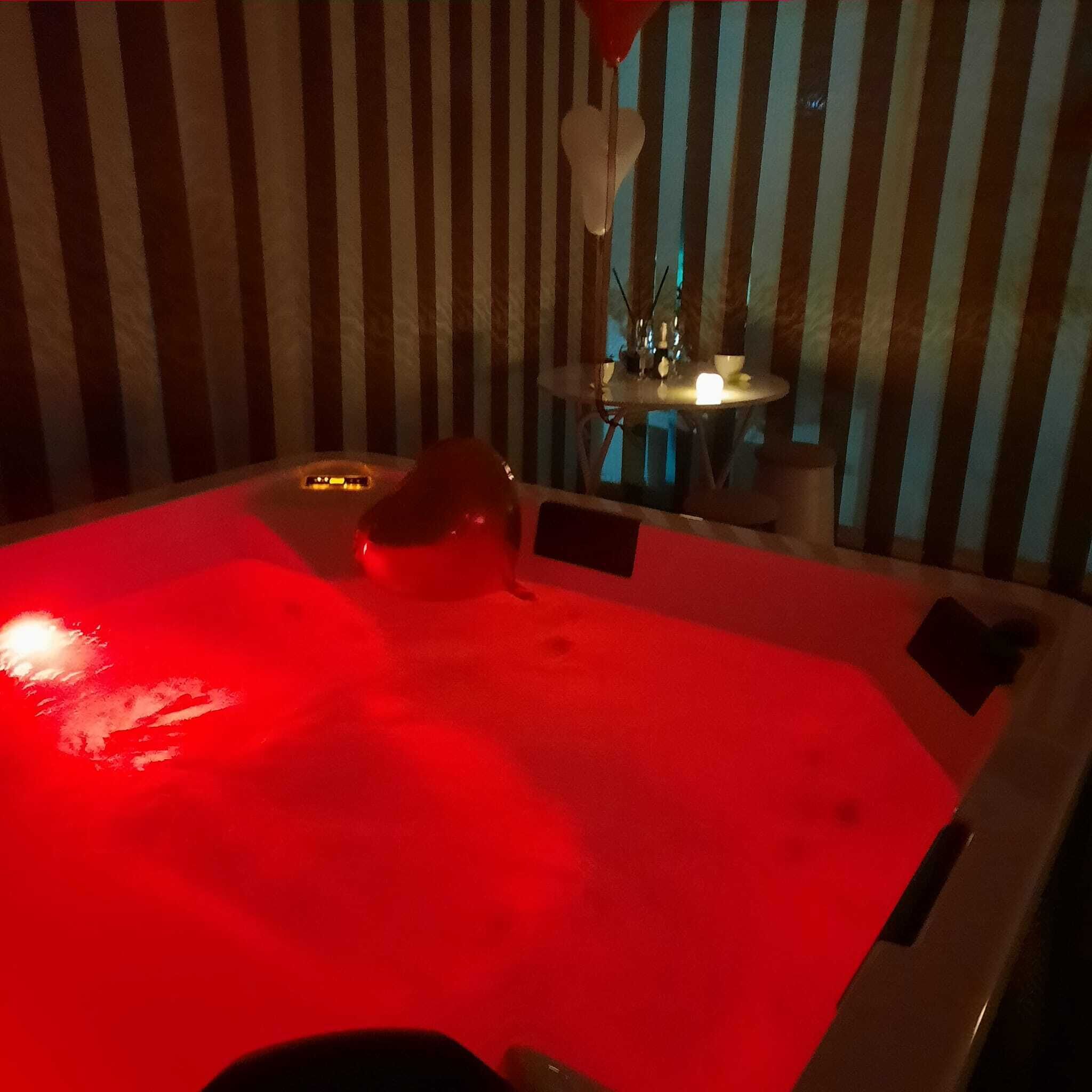 A hot tub with a red light, a small table with a candle, and striped wallpaper.