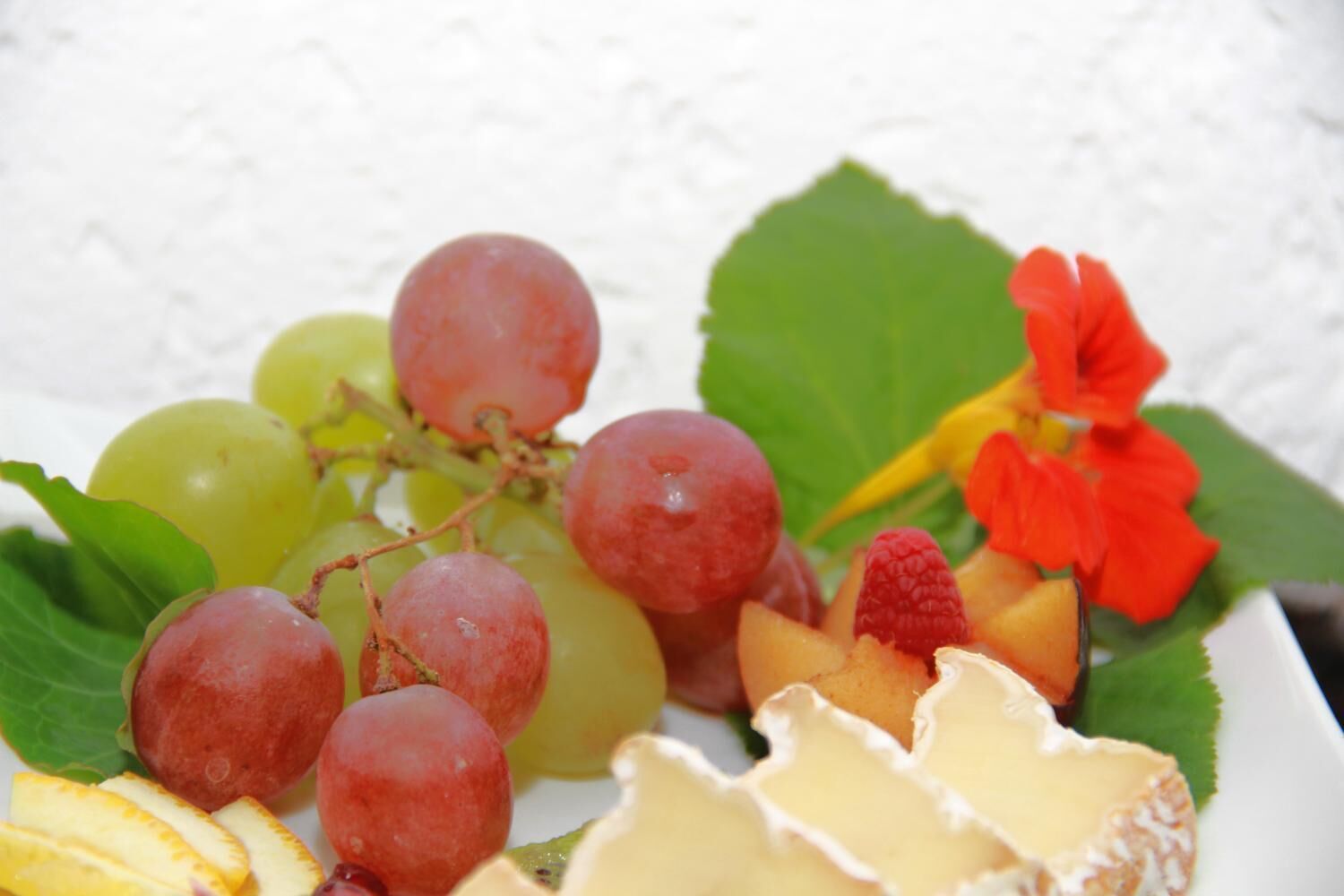 Una bandeja de frutas con uvas, fresas y lonchas de queso.