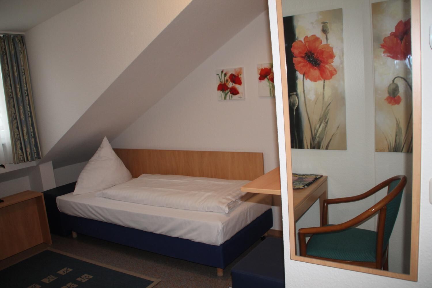 Un dormitorio con una cama, un escritorio y una silla. Hay pinturas en la pared.
