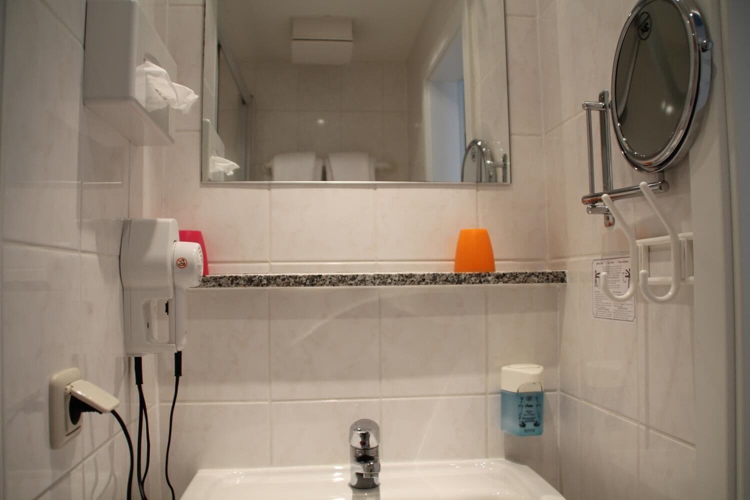 Une salle de bain avec un lavabo blanc, un miroir, un distributeur de serviettes et un distributeur de savon.