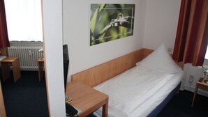 A single bed with a wooden headboard, a bedside table, a small desk, and a wall-mounted picture of a bird. - Hotel Römerhof by Trip Inn (Hanau)