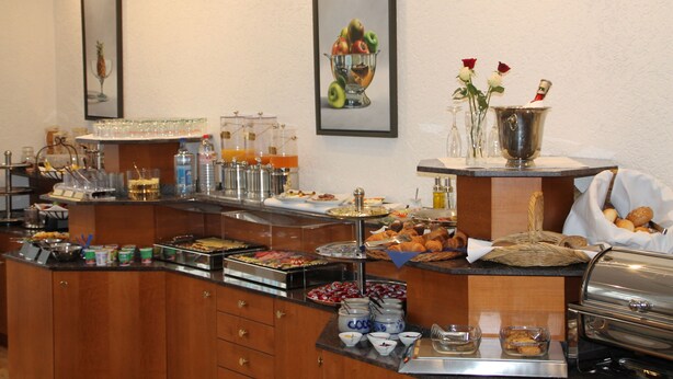 A buffet setup with various food items, beverages, and decorative elements like vases and framed pictures. - Hotel Römerhof by Trip Inn (Hanau)