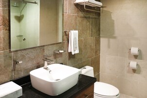Un baño con lavamanos blanco, cabina de ducha con mampara de vidrio, inodoro y perchero para toallas.