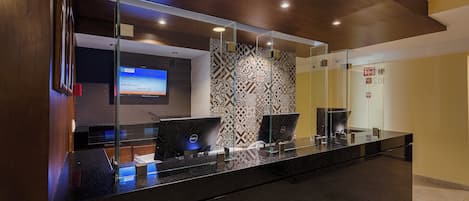 A hotel reception desk with a digital display, glass partitions, and patterned wall tiles.
