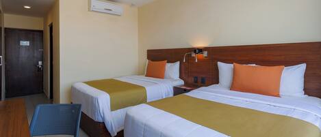 A hotel room with two beds, a wooden headboard, a desk, and a chair.