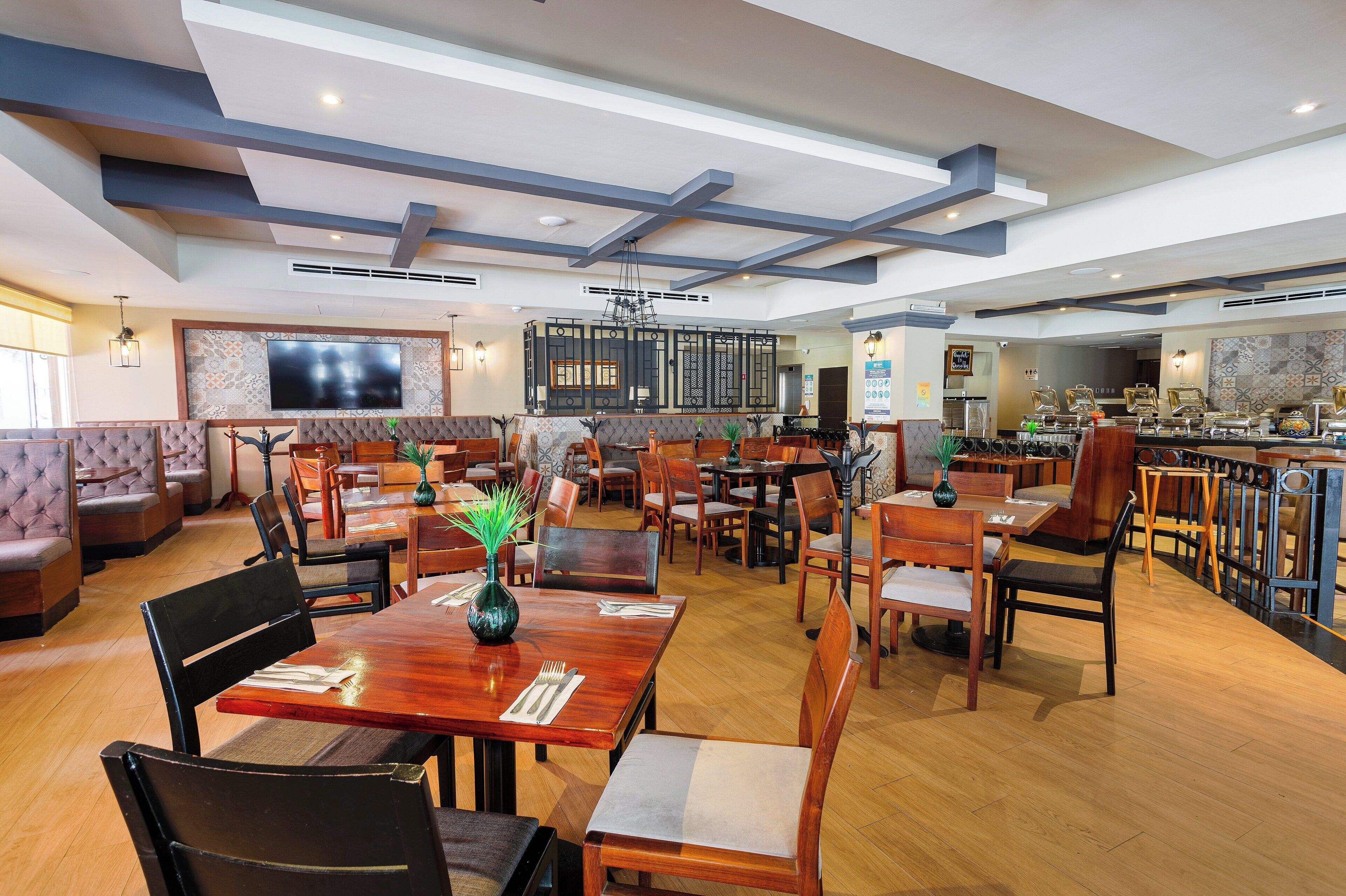 A spacious restaurant with wooden tables and chairs, a large TV screen, and a bar area.