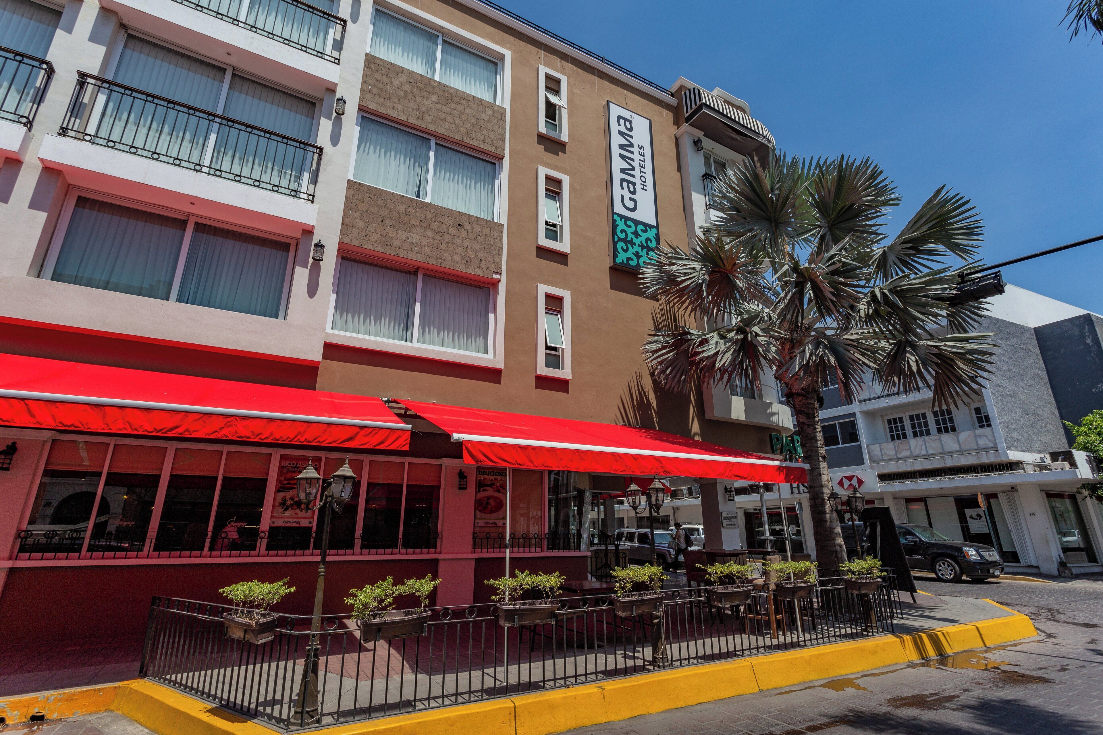Un hôtel avec un auvent rouge et des tables à l’extérieur.